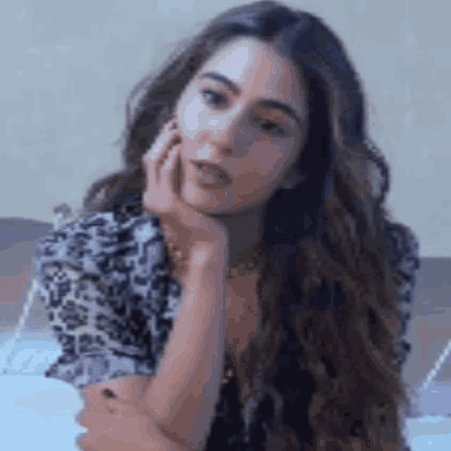 a woman is sitting on a bed with her hand on her face .
