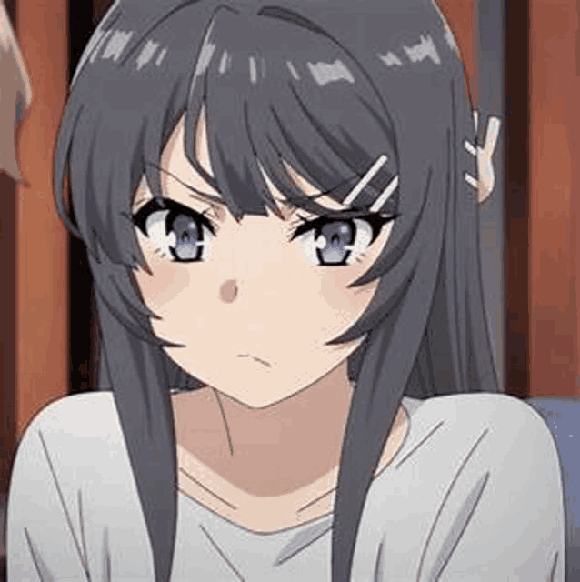 a girl with long black hair and blue eyes is sitting on a couch looking at the camera .