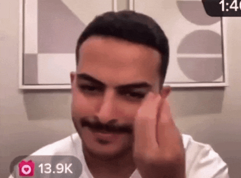 a man with a mustache is wearing a white shirt and has a 13.9k sticker on his face
