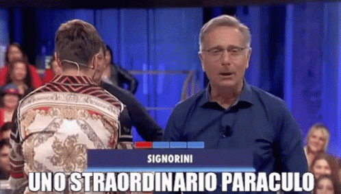 a man is standing in front of a crowd and talking to another man on a television show .