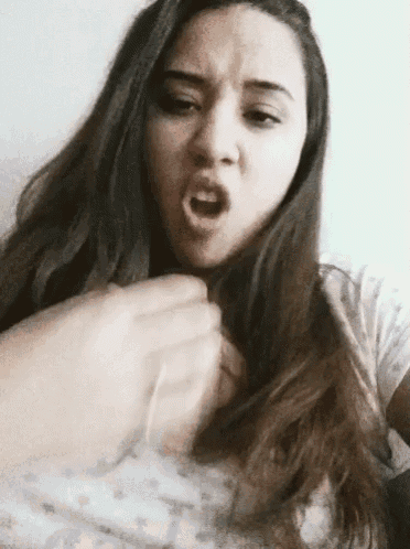 a woman with long hair is making a funny face while holding her hand to her chest .