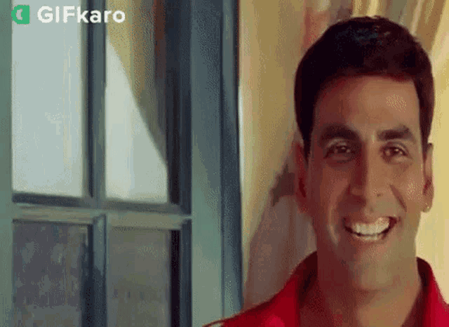 a man in a red shirt is smiling and looking out a window .