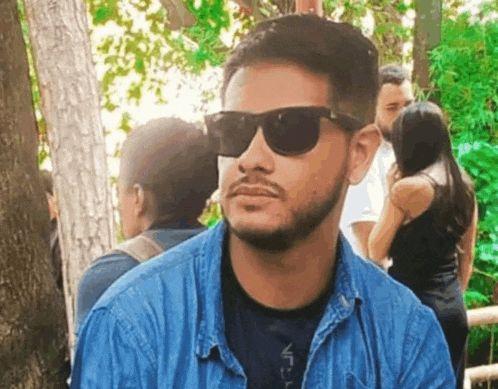 a man wearing sunglasses and a blue shirt is standing in a park