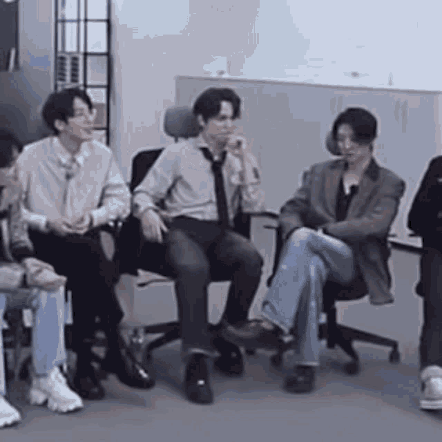 a group of people are sitting in chairs in a room and talking to each other .