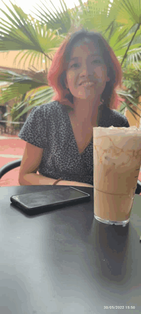 a woman with pink hair sits at a table with a cup of coffee