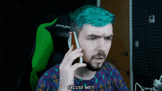 a man with blue hair is talking on a cell phone and says excuse me ?