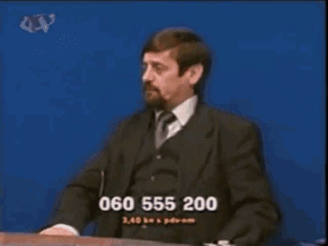 a man in a suit and tie sitting at a desk with a phone number