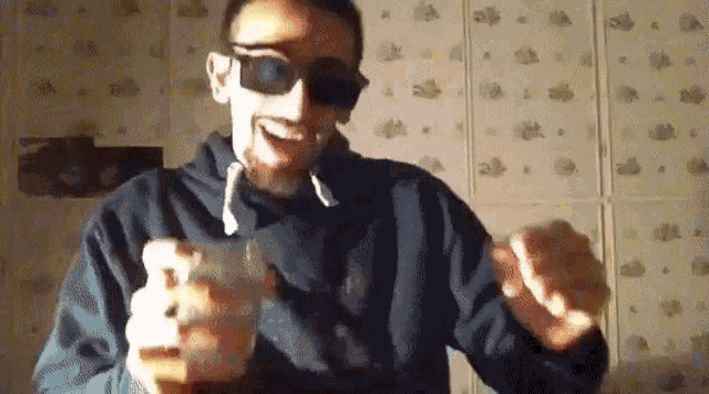 a man wearing sunglasses and a blue hoodie holds a remote control