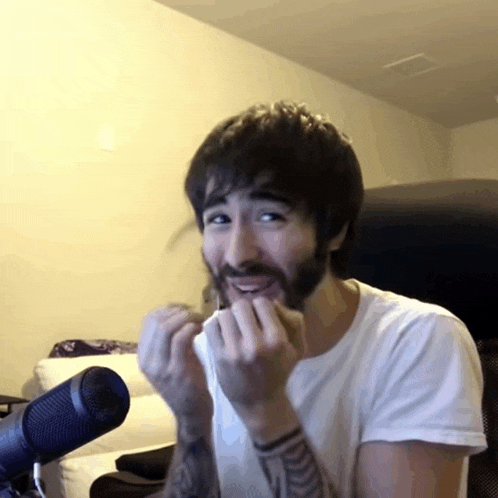 a man with a beard is sitting in front of a microphone with his hands in his mouth