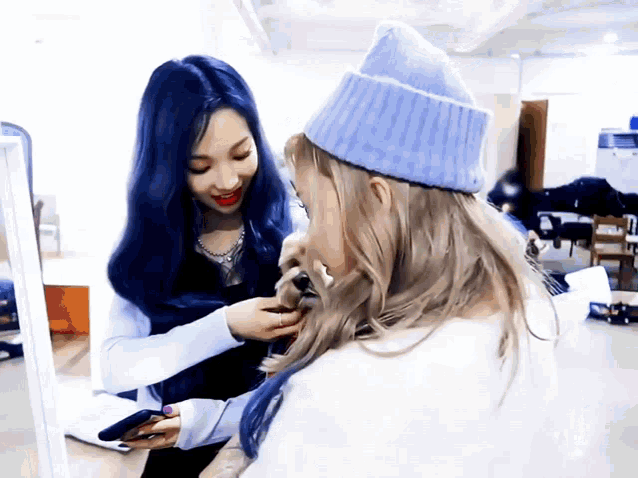 a girl with blue hair is getting her hair done by another girl