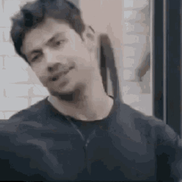 a man in a black shirt is standing in front of a brick wall and smiling .