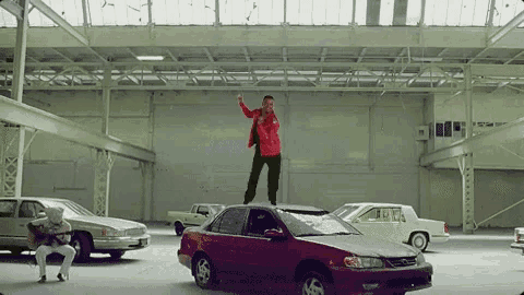 a man is standing on top of a red car .