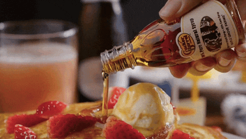 a person pouring maple syrup over a pancake