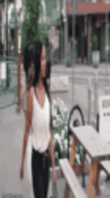 a woman in a white tank top is walking down a sidewalk next to a picnic table .
