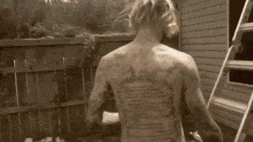a naked man with a lot of tattoos on his back is standing in front of a ladder .