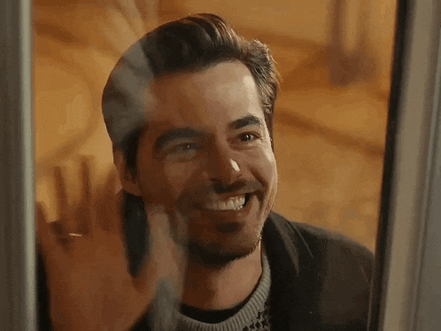 a man with a beard is smiling while looking through a window