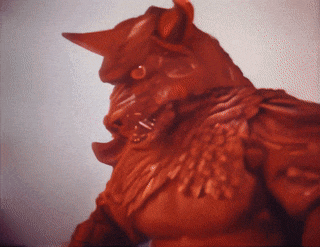 a close up of a red statue with horns and feathers