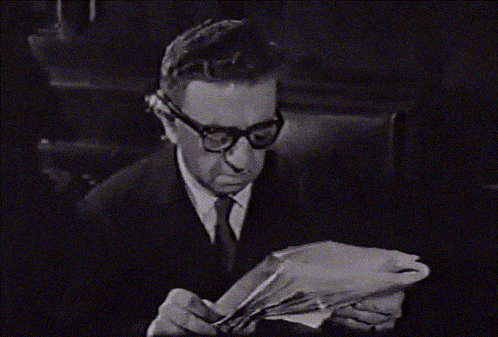 a man wearing glasses is reading a book in black and white
