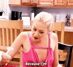 a woman in a pink tank top says because i 'm while holding a spoon .