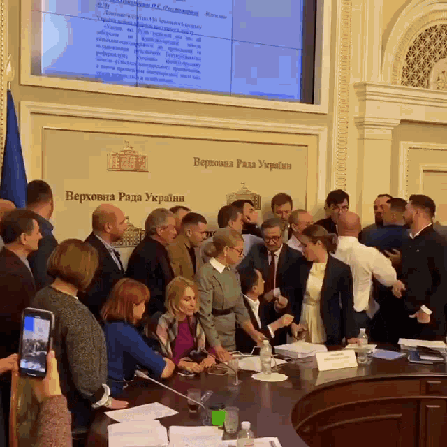 a group of people are gathered in front of a wall that says " верховна рада украïн "
