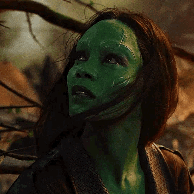 a woman with green paint on her face is standing in front of a tree