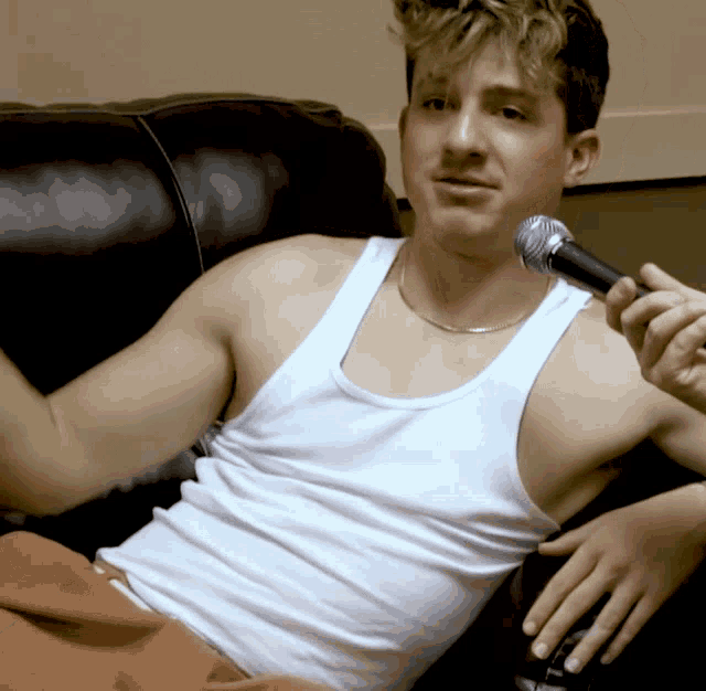 a man in a white tank top is sitting on a couch holding a microphone