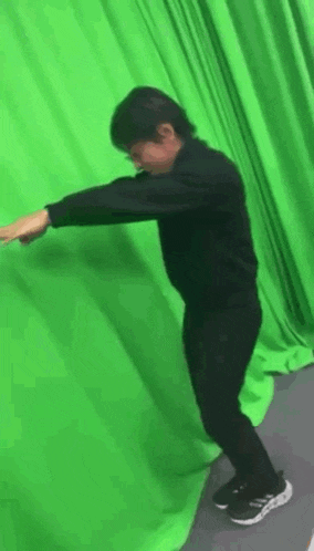 a person is standing in front of a green curtain with their arms outstretched