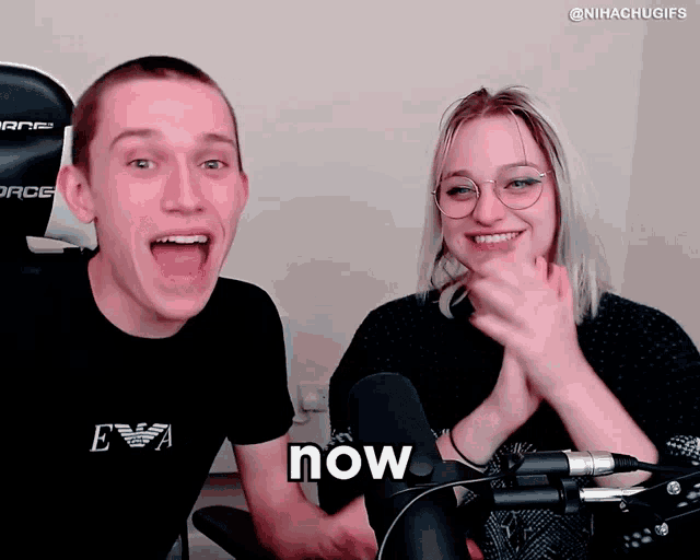 a man and a woman are sitting in front of a microphone with the word now written on the screen