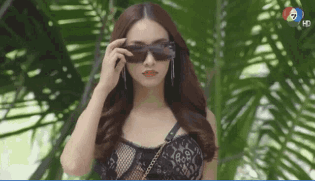 a woman wearing sunglasses stands in front of palm trees