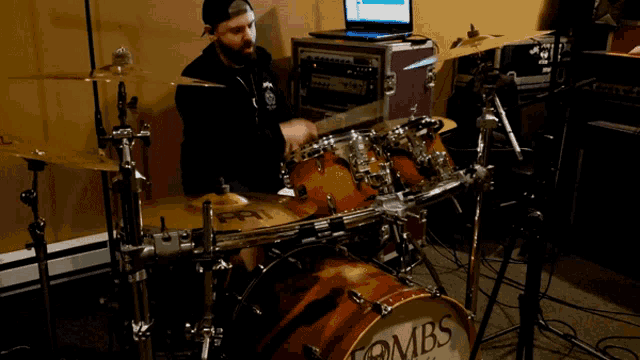 a man playing drums with a laptop in the background and a drum that says bombs on it
