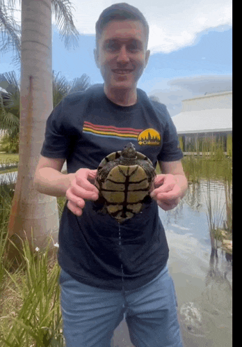 a man wearing a columbia shirt holds a turtle
