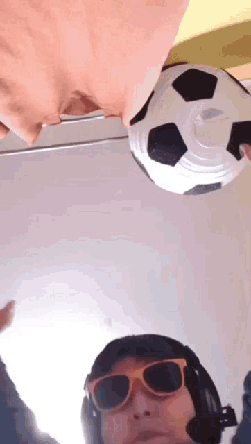 a man wearing sunglasses and headphones looks up at a soccer ball hanging from the ceiling