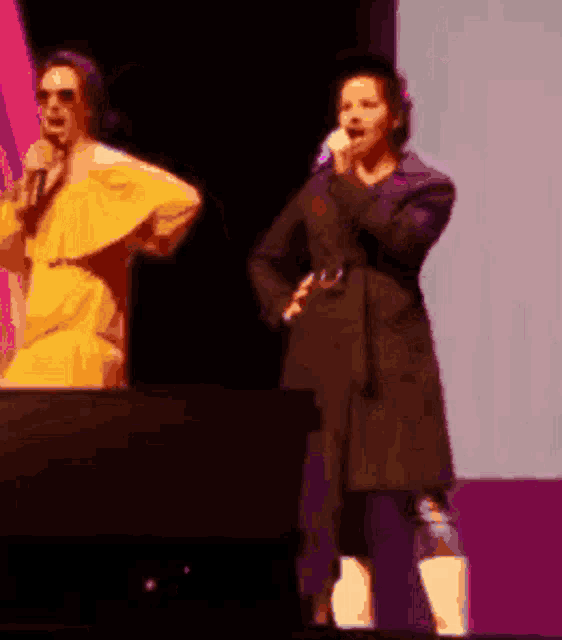 a woman in a yellow dress is singing into a microphone while another woman sings into a microphone .