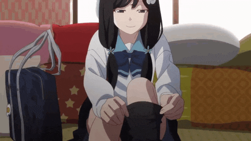 a girl in a school uniform sits on a bed tying her socks