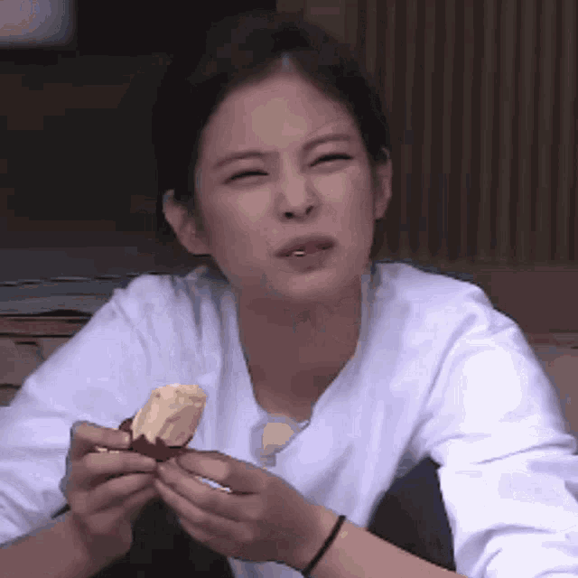 a woman in a white shirt is holding a piece of food and making a funny face