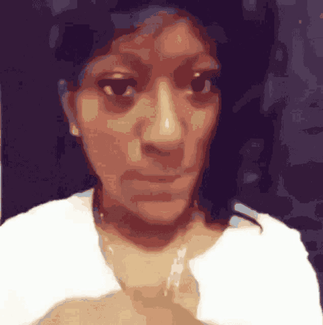 a woman is making a funny face while wearing a white shirt and a gold necklace .
