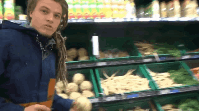 a man in a blue jacket is standing in front of a vegetable aisle in a grocery store
