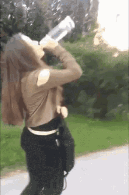 a woman is drinking water from a bottle while standing on a road