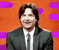 a man in a suit and tie is smiling in front of a purple and orange background .