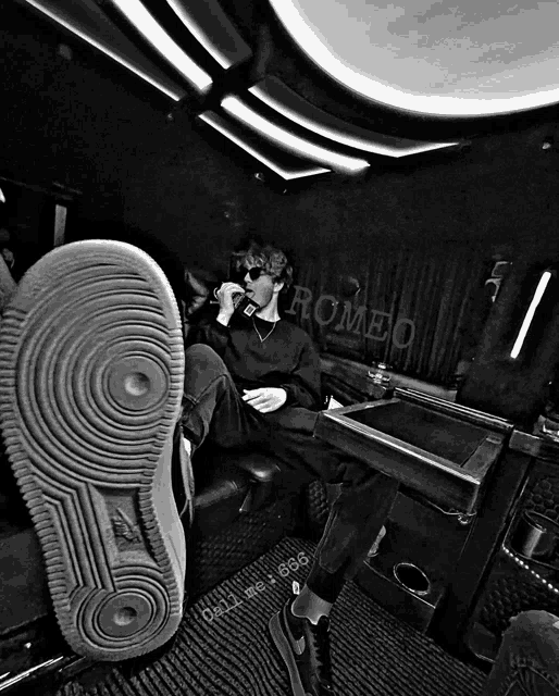 a black and white photo of a man sitting in a room with romeo written on the wall