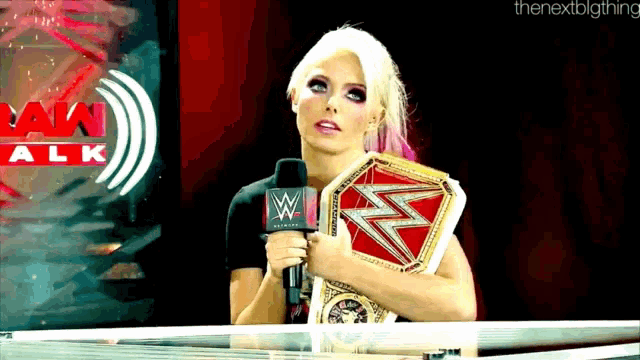 a woman holding a wrestling championship behind a microphone