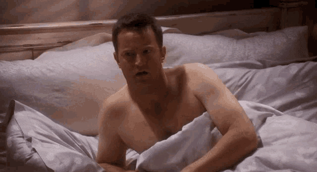 a shirtless man is laying in bed under a white blanket