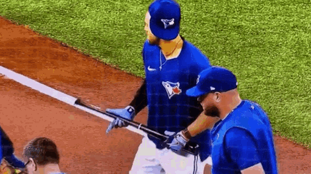 a baseball player in a blue jays uniform is holding a bat on the field .