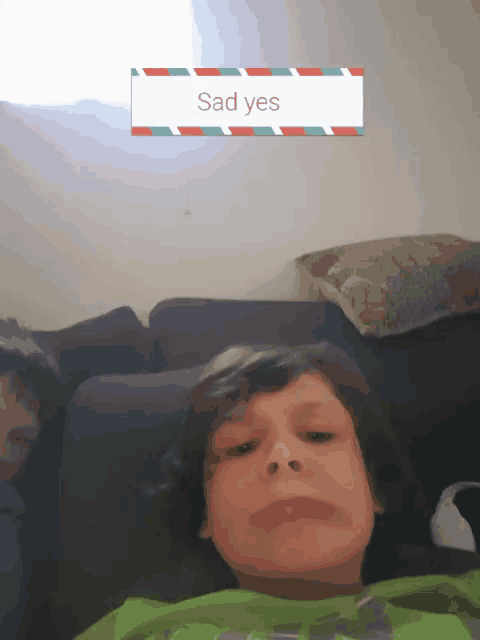 a boy is sitting on a couch with a sad yes sign above him