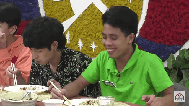 a man in a green shirt is sitting at a table with chopsticks