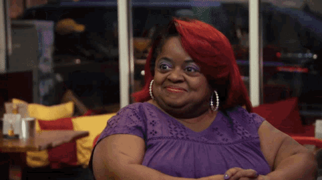 a woman with red hair is wearing a purple shirt and pearl earrings