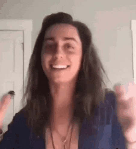 a woman with long hair is smiling and waving at the camera while wearing a blue jacket .