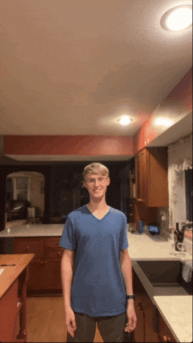 a young man standing in a kitchen wearing a blue shirt