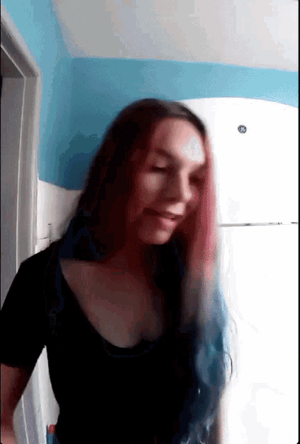 a woman with red and blue hair is standing in front of a refrigerator