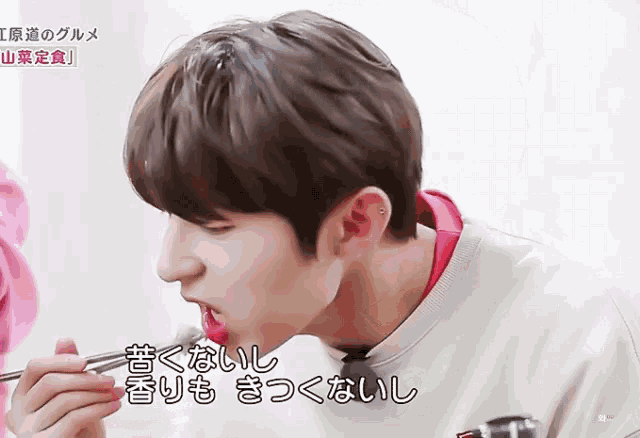 a close up of a person eating with chopsticks with chinese writing behind him